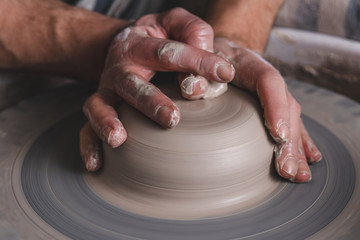 Potter making a new product of white clay on the potter's wheel circle in studio, concept of creativity and art, horizontal photo