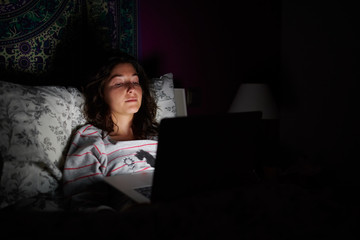 Woman lying in bed with laptop in darkness