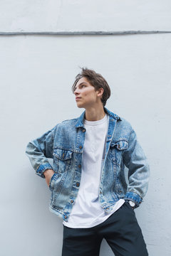A young man stands against a gray wall