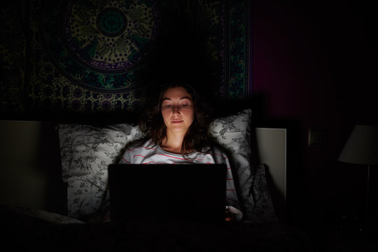 Woman browsing laptop in dark bedroom