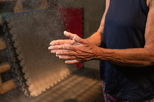 An anonymous fit woman in her seventies claps chalk off of her hands while working out at a gym.