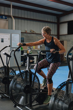 A fit woman in her seventies exercises on a stationary bike in a gym.
