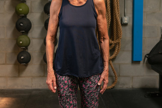 An anonymous fit woman in her seventies stands confidently in a gym.