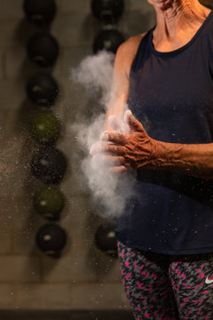 An anonymous fit woman in her seventies claps chalk off of her hands while working out at a gym.