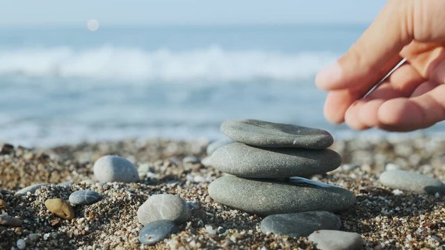 Male hand making a pyramid from pebble stones on the sandy beach. Zen meditation background. Concept of meditation and relax 4K UHD