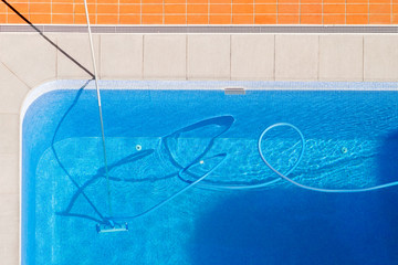 utility worker cleaning the swimming pool with vacuum equipment