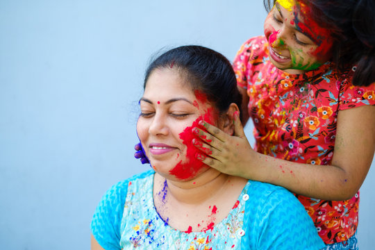 Little girl smearing color powder on her mothers face during holi celebration