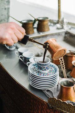 Person pouring coffee in cup from cezve