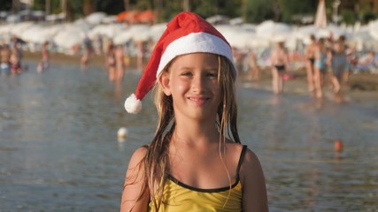 Little adorable girl in red Santa hat having fun at beach.