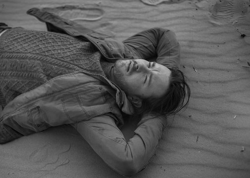 black and white portrait of a handsome manly man lying on the sand in a jacket and sweater