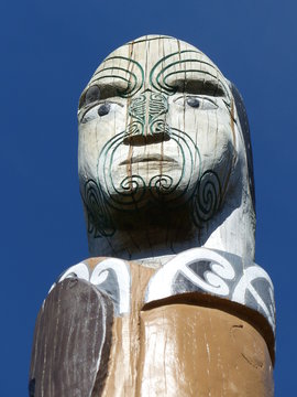 head of a maorie statue Maori carving on wood, wood piece in grass with a blue sky, hawke's bay region, new zealand