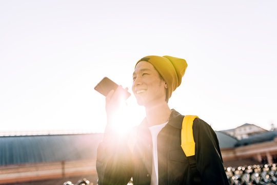 Young Asian Man Talking On Phone While Standing Besides A Bicycle Parking