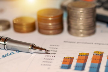 Pens and coins placed on financial reports or stock market graph analysis.