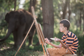 Asian boy with Down's syndrome is happily drawing a picture of an elephant in the garden.Drawing,...