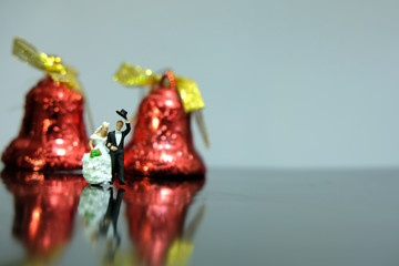 Miniature wedding concept - bride and groom walking on shiny floor with bell ornament