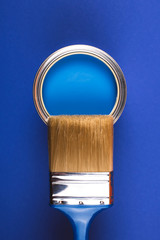 Brush on open can of blue paint on blue background. Color of the year in interior.