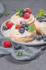 Mini pavlova meringue cakes with fresh raspberries and blueberries with mint leaves.