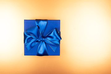 Blue present box with bow on golden background with sparkles.
