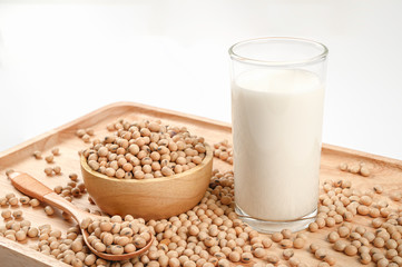Soy milk in glass with soy beans in wooden bowl and spoon on white background