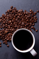 Roasted coffee beans and cup of coffee on granite background