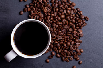 Roasted coffee beans and cup of coffee on granite background