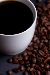 Roasted coffee beans and cup of coffee on granite background