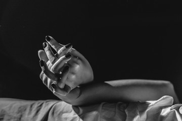 Close up on female young woman's girl's beautiful hands woman lying on the bed black and white nail polish in dark room crossed fingers on sheet gentle passion love temptation emotion concept - obrazy, fototapety, plakaty