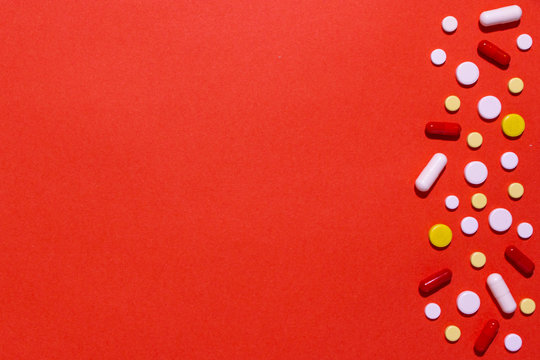 pills and capsules of different shapes and colors on a red background.