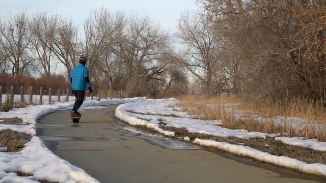 Mature man is commuting on an electric skateboard along bike trail in winter scenery - Colorado Front Range Trail in Boyd Lake State Park