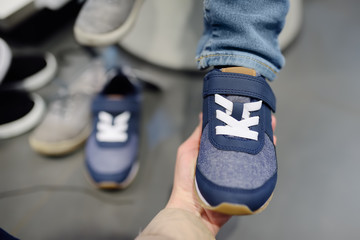 Little boy during shopping with his mother. Kid trying new fashion seasonal sneakers.