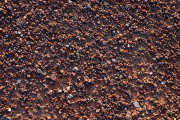 Coarse red metal ore rich gravel and sand, flat surface in hard sunset light, resemblance to Mars surface.