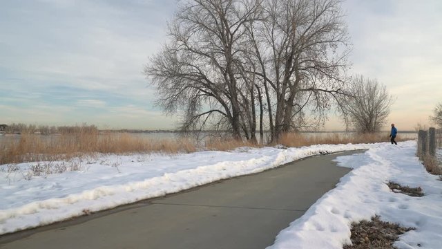 Mature man is commuting on an electric skateboard along bike trail in winter scenery - Colorado Front Range Trail in Boyd Lake State Park