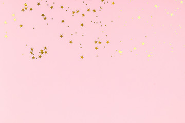 Golden stars glitter confetti on pink background. Festive backdrop.