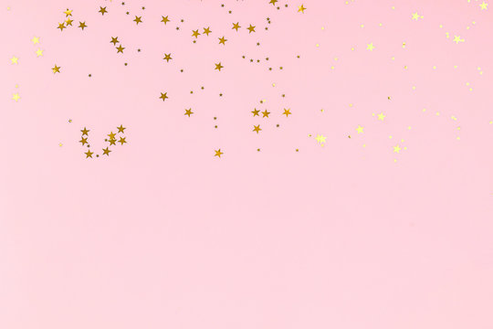 Golden stars glitter confetti on pink background. Festive backdrop.