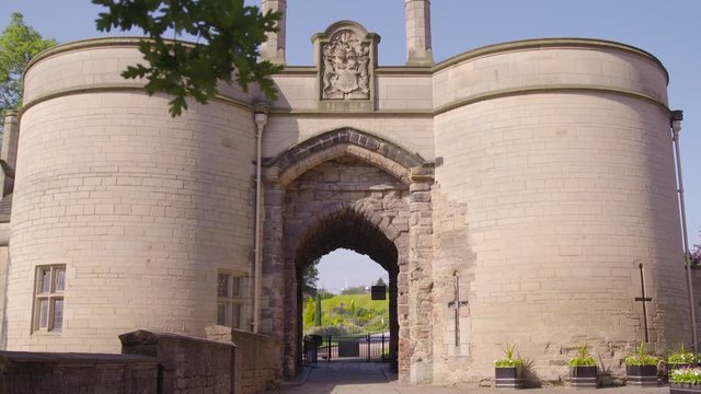 A wide, medium-long shot of the arched pathway of Nottingham Castle composed of two round buildings made of stone and bricks topped with a carved crest.