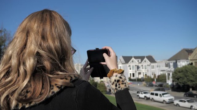 Young woman tourist taking photo with smartphone of Painted Ladies San Francisco