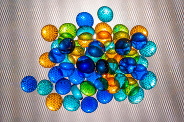 Multicolored oval and round pieces of glass are illuminated through a textured background