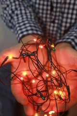 Fototapeta na wymiar Close up of shining Christmas lights in hands of a man, miracle and winter holidays concept. Beautiful glowing garland in male hands.