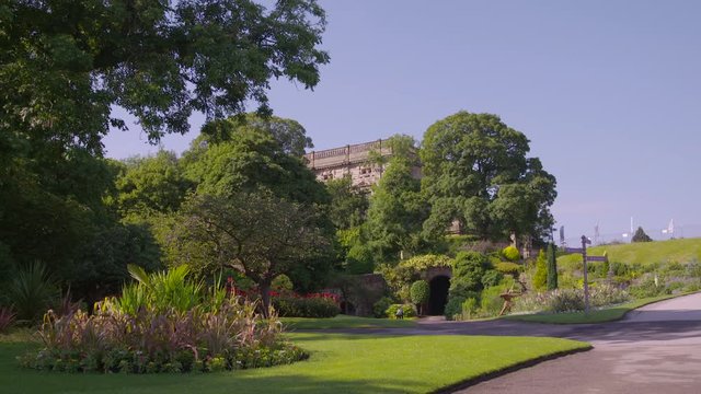 A wide, medium-long-shot of a tunnel entrance leading to an aged structure beyond the curated and lush garden by the roadside.