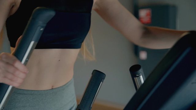 slim sportive young woman in gym doing exercises on elliptical trainer working out closeup. cardio workout. concept of effort, sportive, shape, fitness, millenial, lose weight.