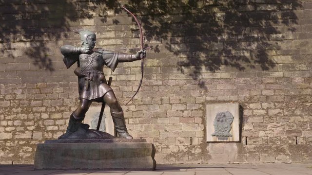 A wide, steady shot of the monument of Robin Hood made of metal located in Nottingham, England, against an aged brick wall.