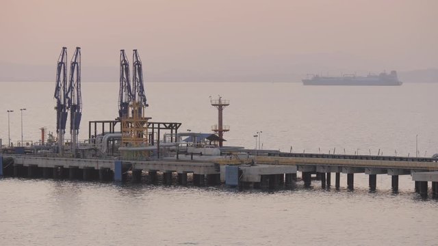 Jetty of iquefied gas terminal with large LNG tanker on horizon of sea in evening