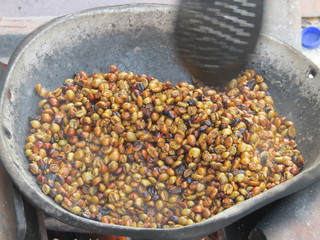 Traditional process of making roasted coffee bean menggoreng kopi. roasting beans in big pan on a wood-burning stove with firewood stir with large aluminum scoop utensil. Turn green seeds into black.