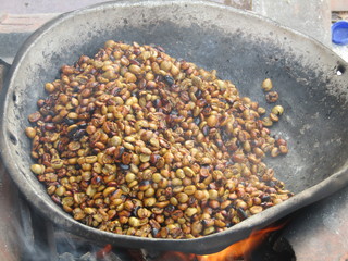 Traditional process of making roasted coffee bean menggoreng kopi. roasting beans in big pan on a wood-burning stove with firewood stir with large aluminum scoop utensil. Turn green seeds into black.