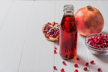 Glass bottle of pomegranate juice with ripe pomegranate fruits on a white table.