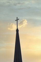 cross up on the top of church steeple against cloudy sky in background