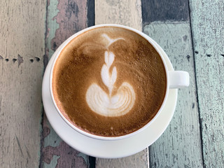 Coffee in a white cup and saucer with a beautiful Latte Art on a pastel wood table and a vintage pattern on the top view.