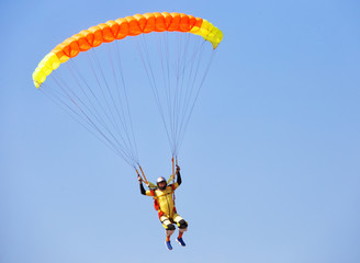 Skydiver under orange dome of a parachute in cloudless sky