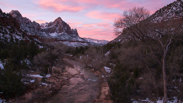 Colorful sunrise from the Zion bridge with the sky lit up looking down the Virgin River towards The Watchman peak covered in snow in winter.