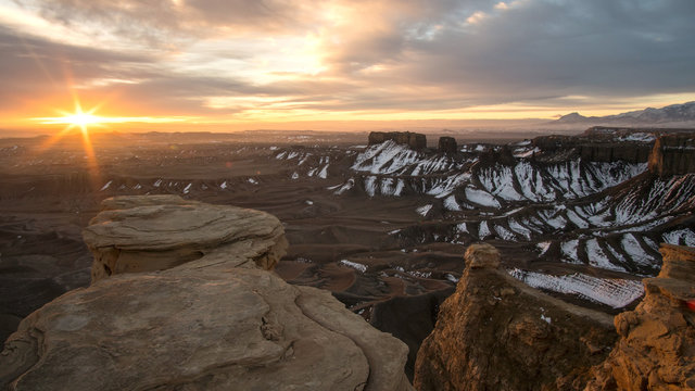 Sun peaking through the clouds lighting up the desert at sunrise from canyon overlook in the Utah badlands.